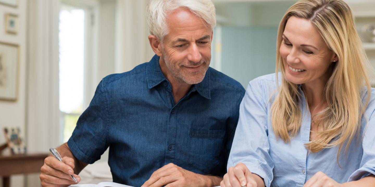 man and women looking at documents smiling at dining table holding pens